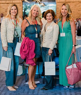 Four women posing together at an event, each holding their Retreats Resources goodie bag
