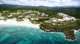 Aerial view of the large Susurros del Corazón beachfront resort complex with pools, white sand beach, and turquoise water, surrounded by lush green hills.