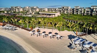 The Etéreo beachfront resort with modern buildings, palm trees, sun loungers, and umbrellas arranged on a sandy beach beside clear blue water.