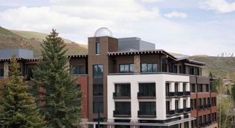 The Observatory Sun Valley, a Viceroy Resort - Ketchum, ID - A modern multi-story building with a mix of wood and white exterior finishes, large windows, and balconies, set against a backdrop of hills and trees.