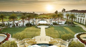The large Waldorf Astoria Monarch Beach Resort & Club luxury resort with palm trees, a swimming pool, manicured lawns, and white buildings, overlooking a golf course and the ocean at sunset.