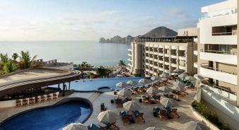 Corazon Cabo Resort & Spa, Cabo San Lucas,  with an outdoor pool, sun loungers, and umbrellas overlooks the ocean and distant rocky hills under a partly cloudy sky.