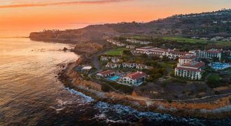 Aerial view of the coastal Terranea Resort with red-tiled roofs, surrounded by cliffs and ocean at sunset.