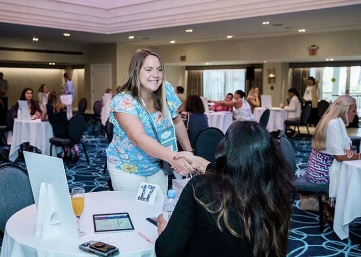 A man in glasses and a plaid shirt shakes hands with a woman with a floral tattoo on her arm during a Retreats Resources Lone Star State Roadshow.