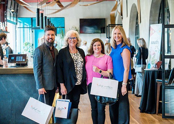 Four smiling attendees holding Retreats Resources goodie bags at a roadshow.