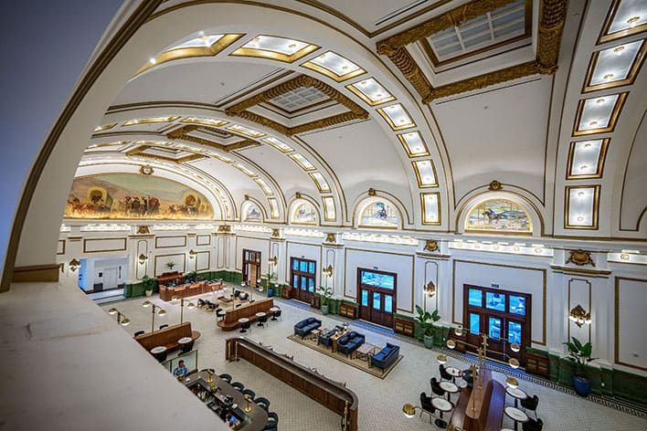 Asher Adams’ large, elegant hotel lobby with arched ceilings, ornate gold details, murals, and multiple seating areas, viewed from an upper level.