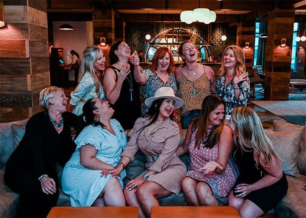 A group of ten women sitting and standing in a lounge area, laughing and interacting with each other.