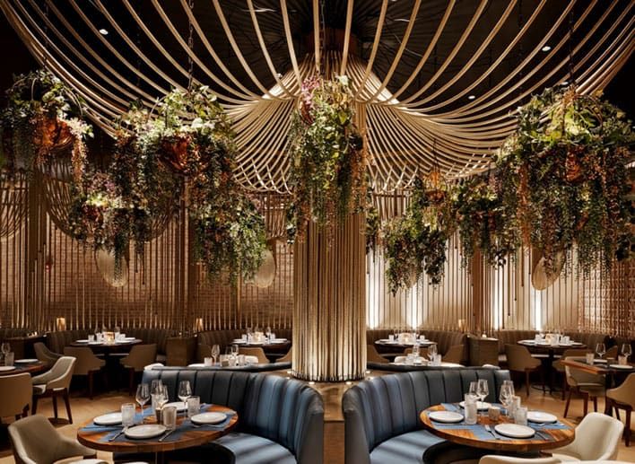 Inside Mission Ceviche Union Square – a modern restaurant interior with circular booths, blue cushioned seating, round tables set for dining, and hanging greenery under decorative ceiling rods.